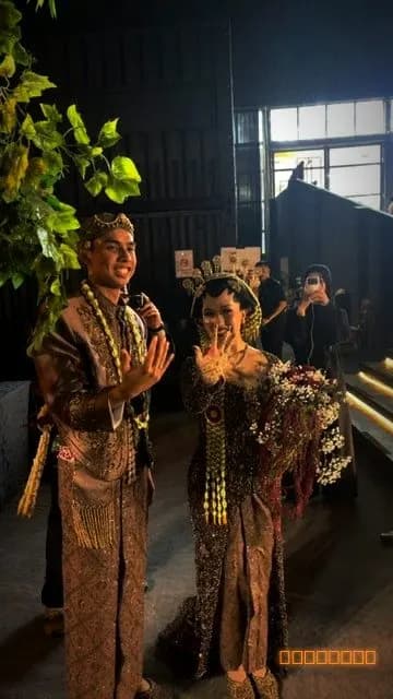 A couple in traditional attire waving at a guest's camera